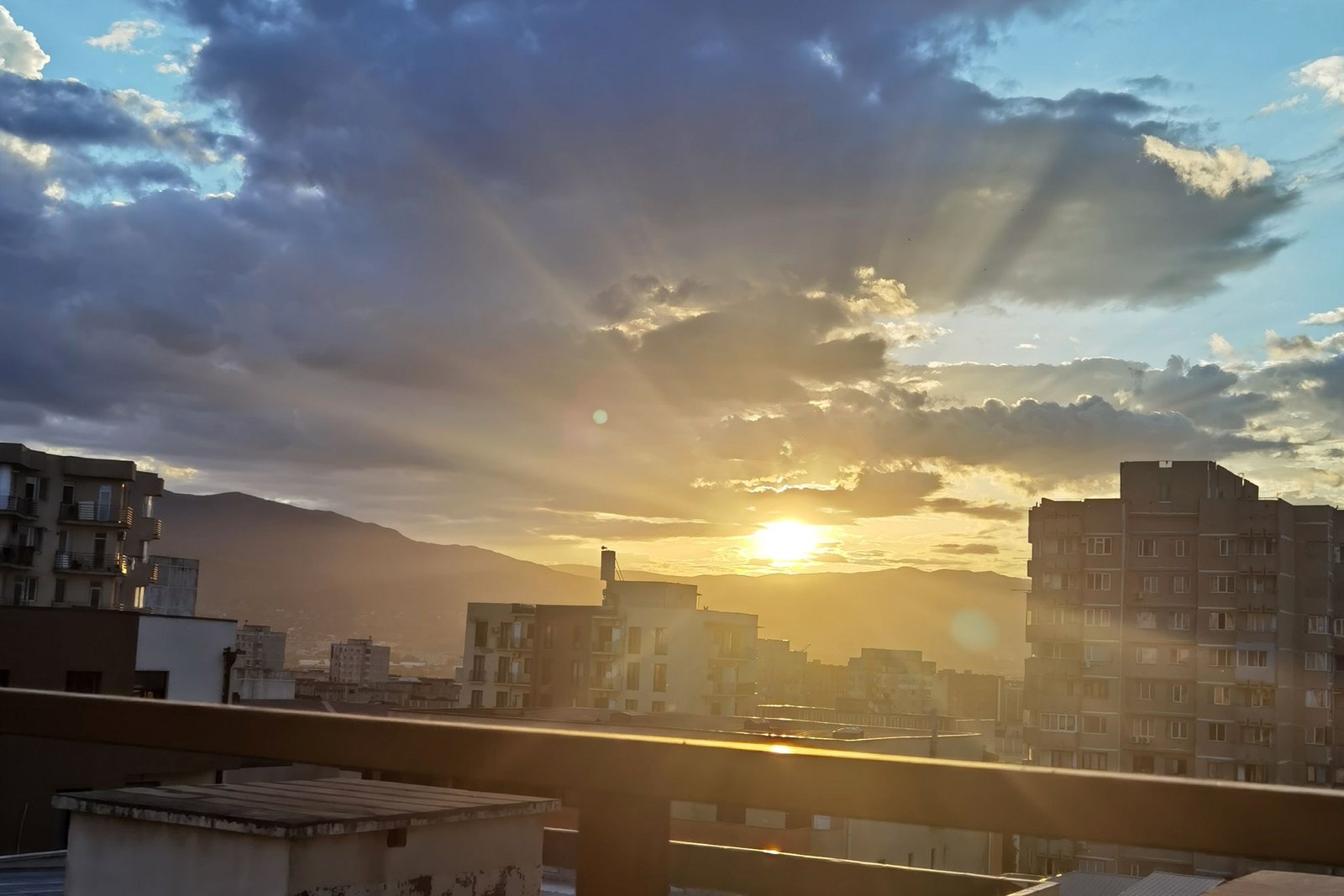 Blick von unserer Terrasse über Tiflis, die Sonne zwischen Wolken über den Bergen